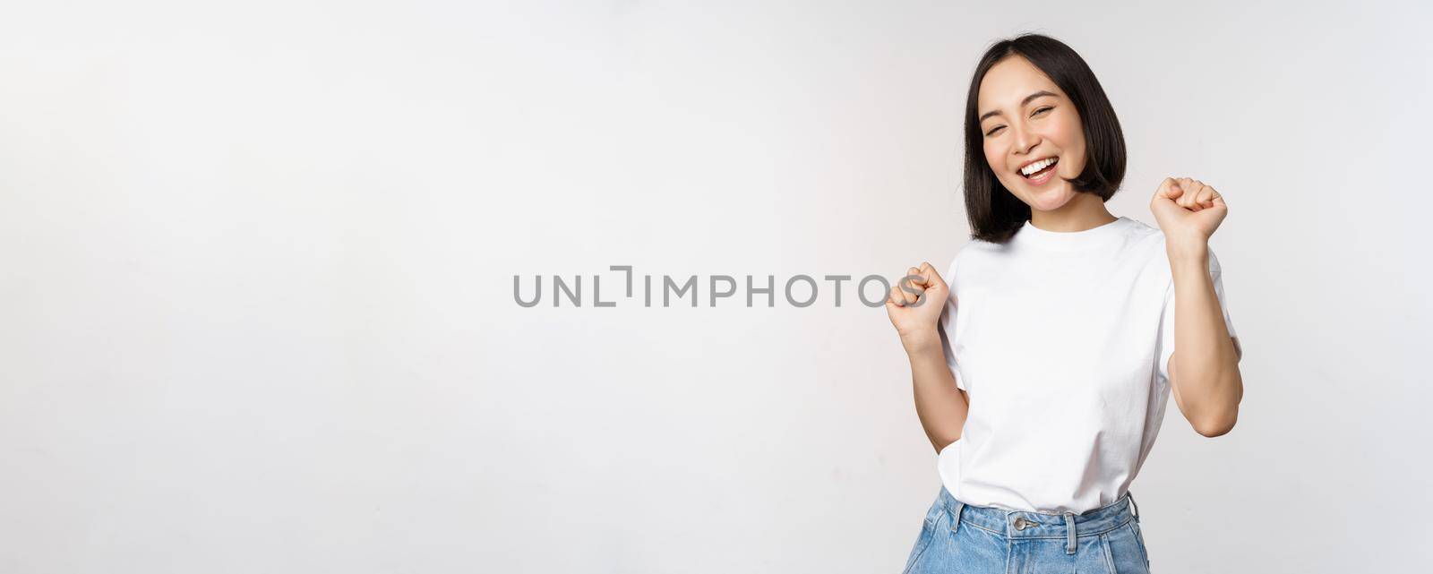 Happy dancing korean girl posing against white background, wearing tshirt by Benzoix