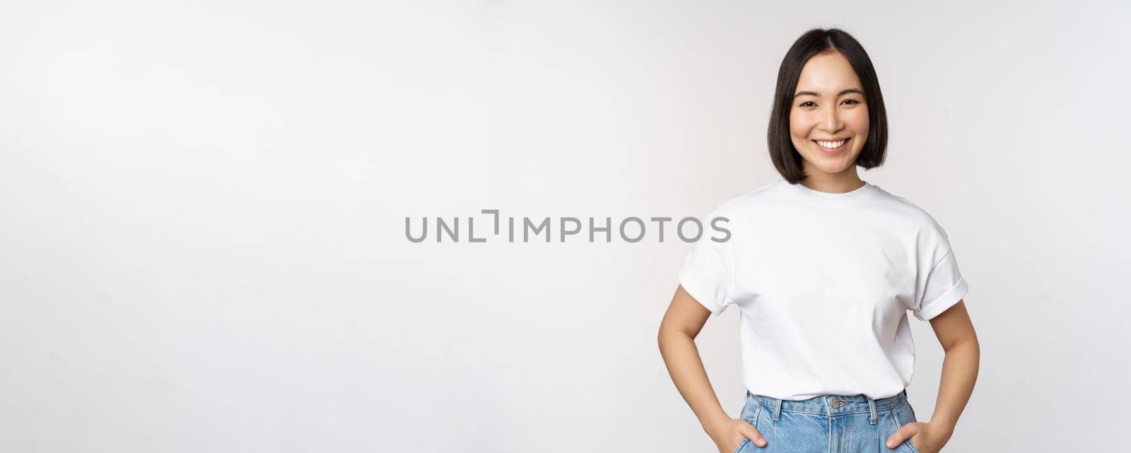 Lifestyle. Happy modern asian girl, smiling and looking happy at camera, posing in white tshirt and jeans, studio background.