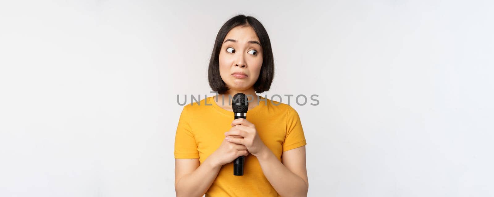 Modest asian girl holding microphone, scared talking in public, standing against white background by Benzoix