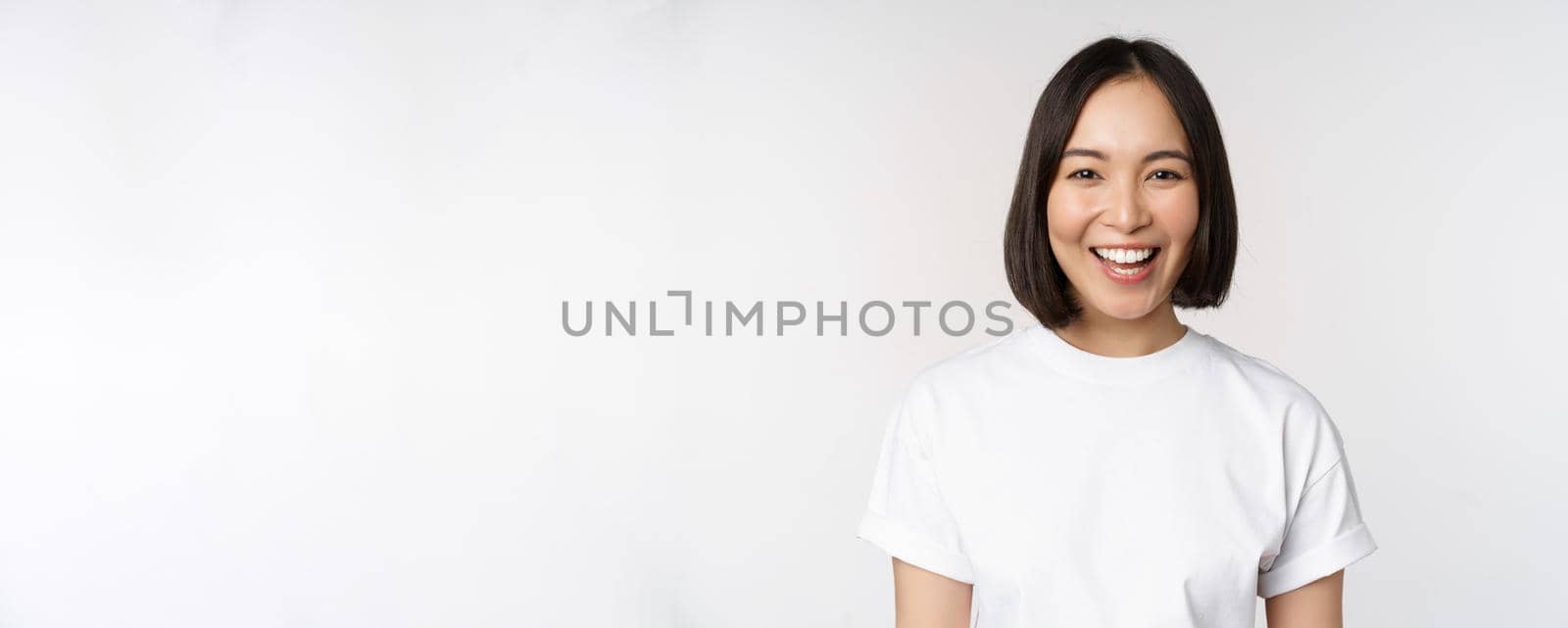 Close up portrait of young asian woman looking at camera, wearing t-shirt, smiling and looking happy, white background.