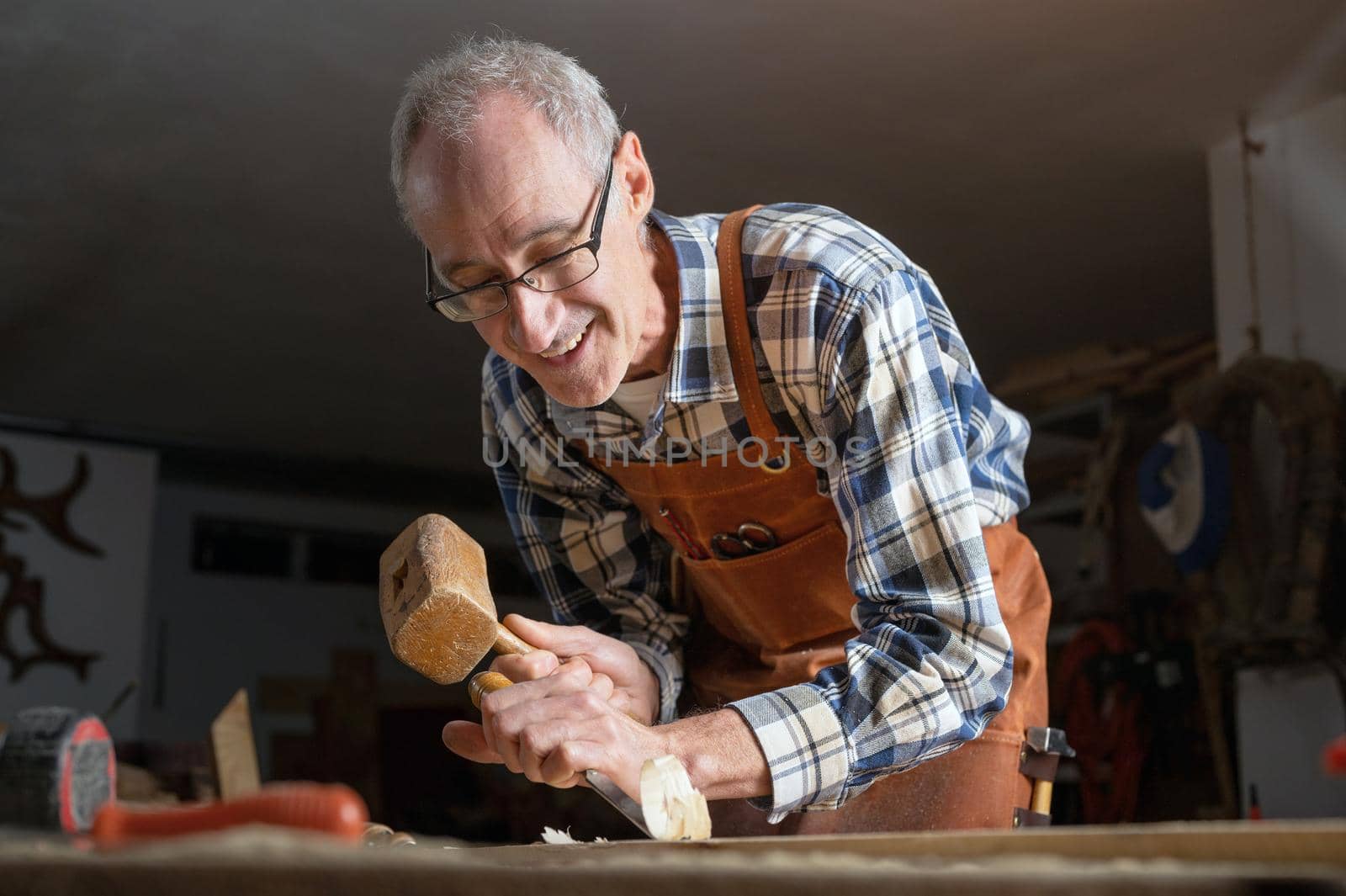 Skilled carpenter carving wood with hammer and chisel by HERRAEZ