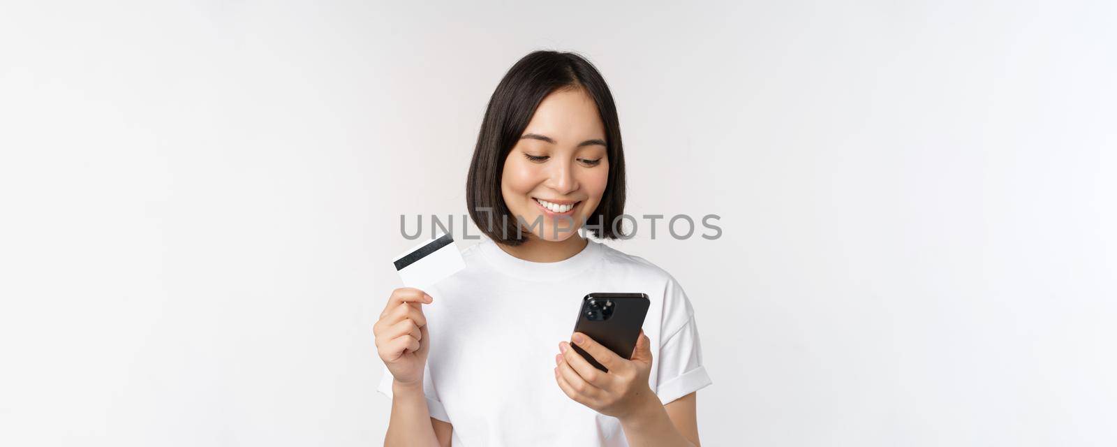 Online shopping. Happy asian woman using credit card and smartphone app, paying on website via mobile phone, white background.