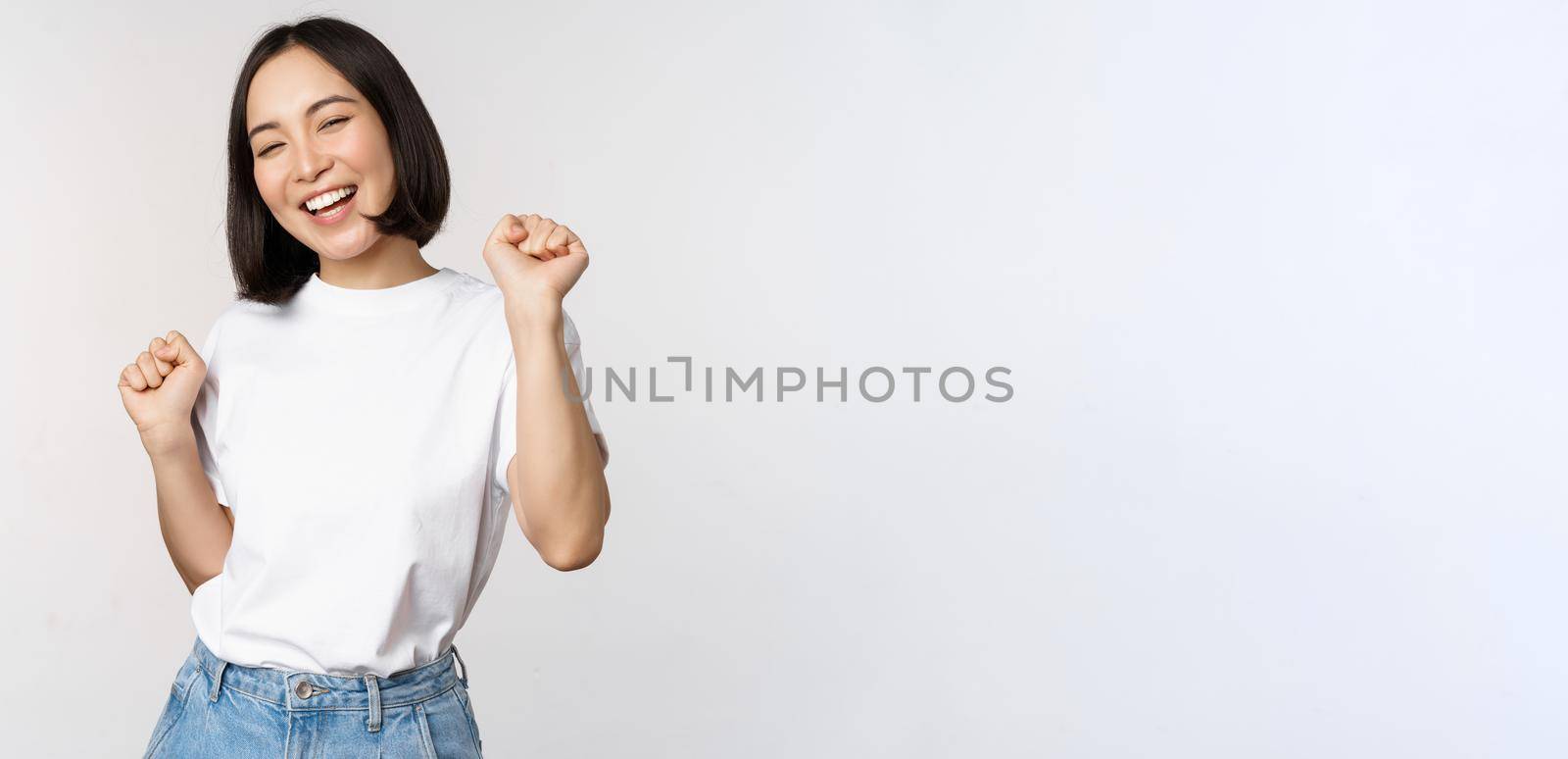 Happy dancing korean girl posing against white background, wearing tshirt.