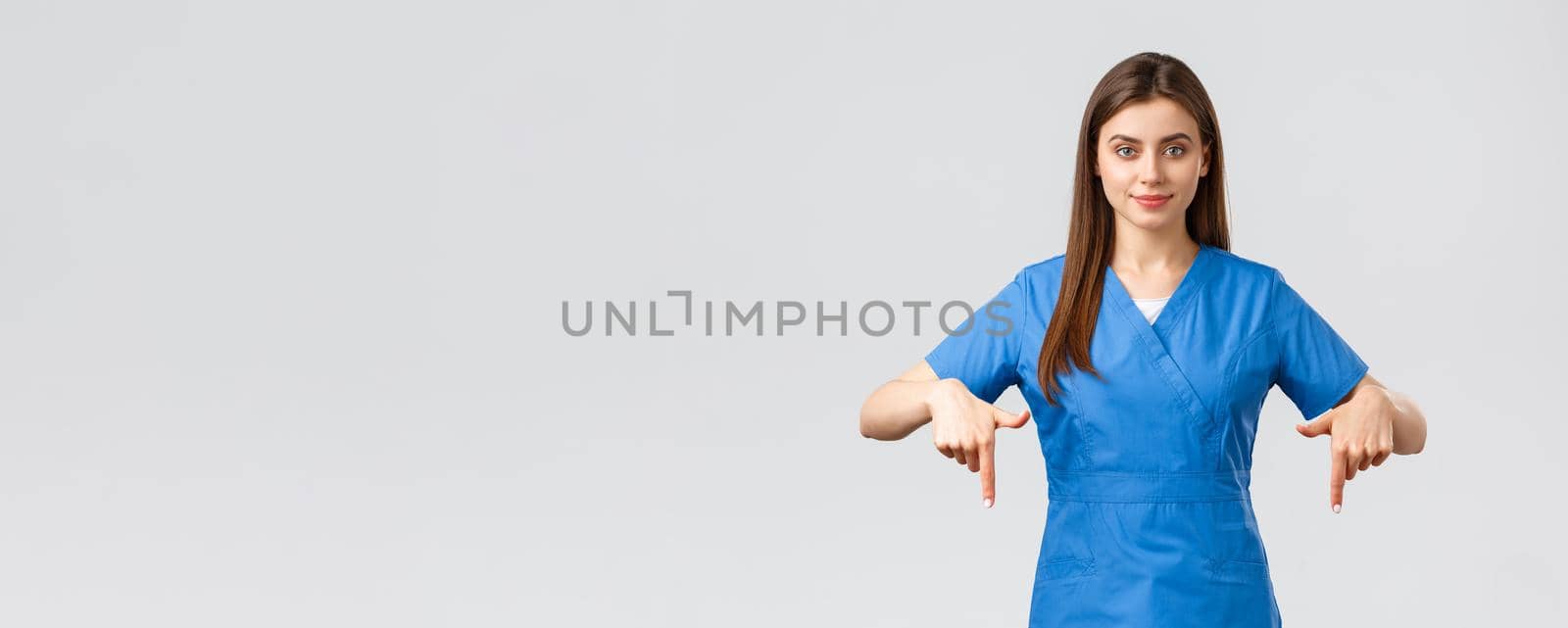 Healthcare workers, prevent virus, insurance and medicine concept. Smiling pretty nurse or doctor in blue scrubs, pointing fingers down, showing patients advertisement, recommend drugstore by Benzoix