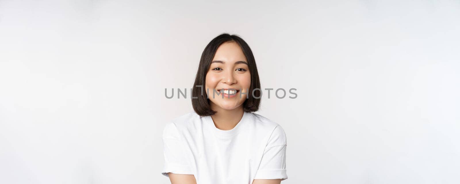 Beautiful korean girl smiling, white teeth, looking lovely at camera, standing in white tshirt over studio background by Benzoix