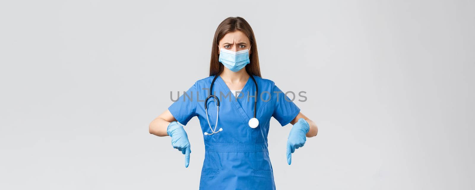 Covid-19, preventing virus, health, healthcare workers and quarantine concept. Concerned and displeased, angry female nurse or doctor feel suspicious, pointing fingers down, wear medical mask.