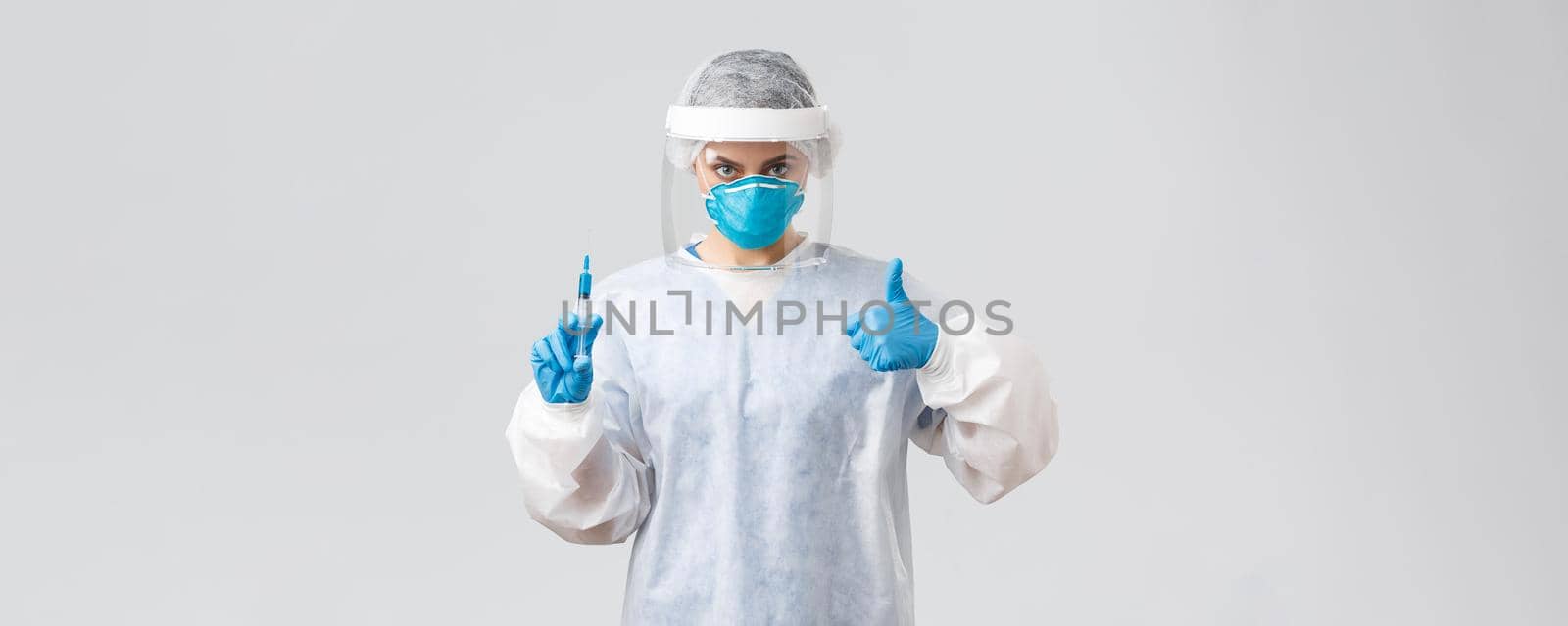 Covid-19, medical research, healthcare workers and quarantine concept. Confident professional doctor in personal protective equipment PPE costume, show thumb-up, hold syringe with corona vaccine.