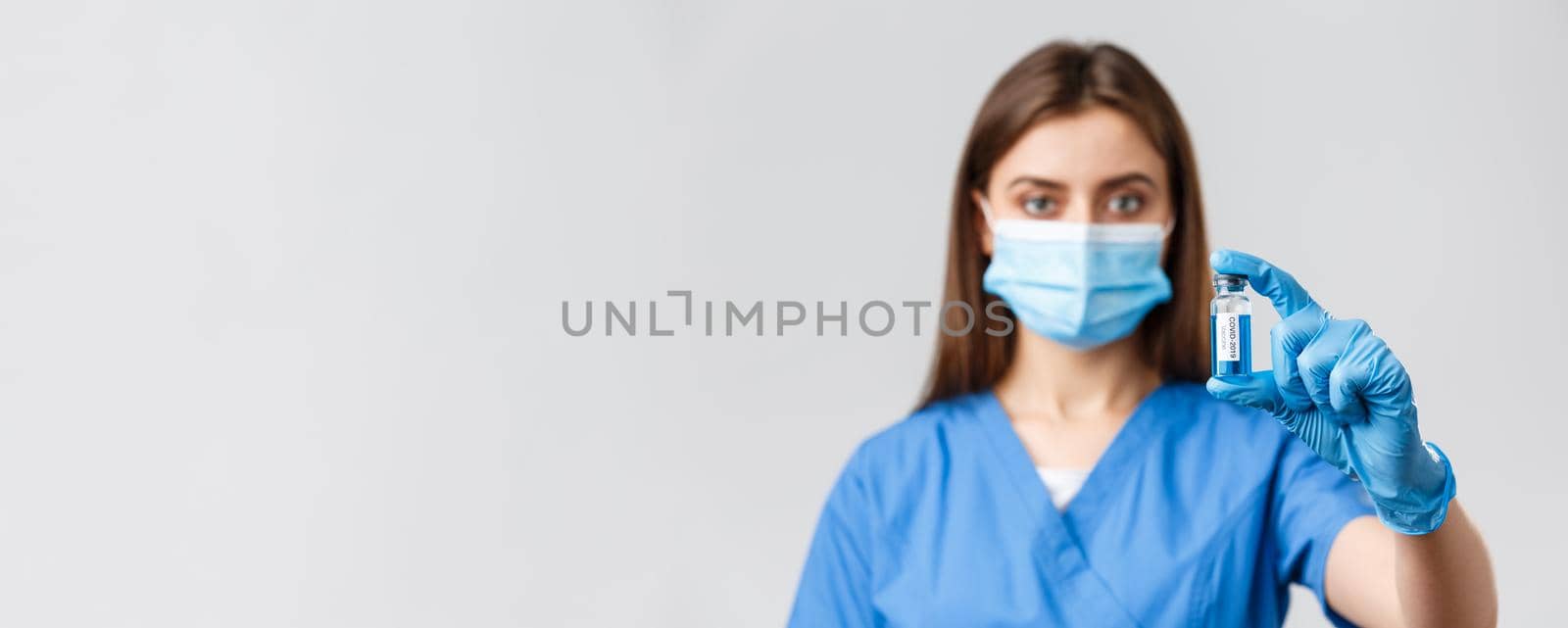 Covid-19, preventing virus, health, healthcare workers and quarantine concept. Close-up of serious-looking young doctor or nurse in clinic, lab showing coronavirus vaccine in ampoule.