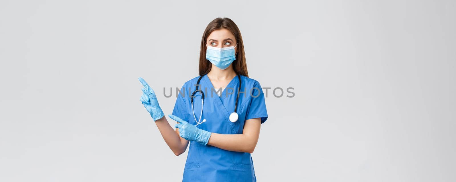 Covid-19, preventing virus, health, healthcare workers and quarantine concept. Doctor, female nurse in medical mask and blue scrubs, looking and pointing left at banner with coronavirus info.