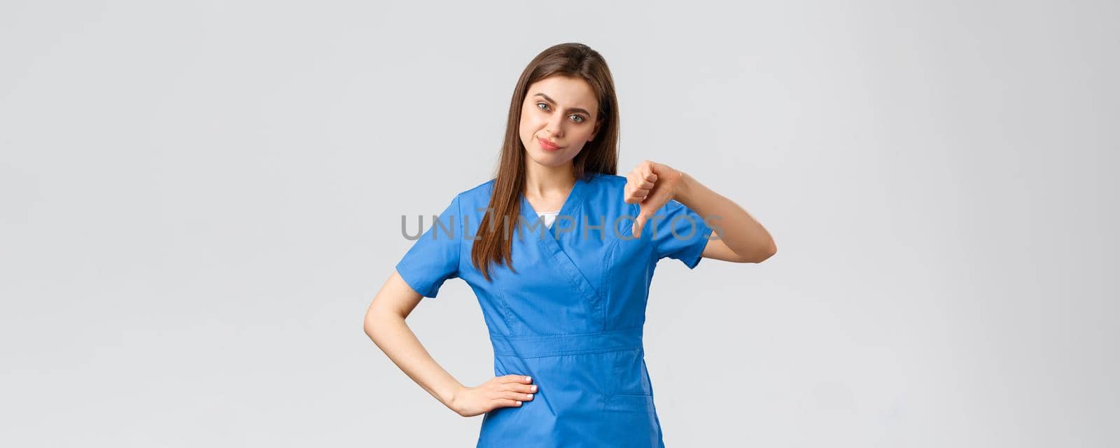 Healthcare workers, prevent virus, insurance and medicine concept. Skeptical and disappointed young female nurse, doctor in scrubs, thumb-down and smirk, rate bad idea, judging awful behaviour by Benzoix