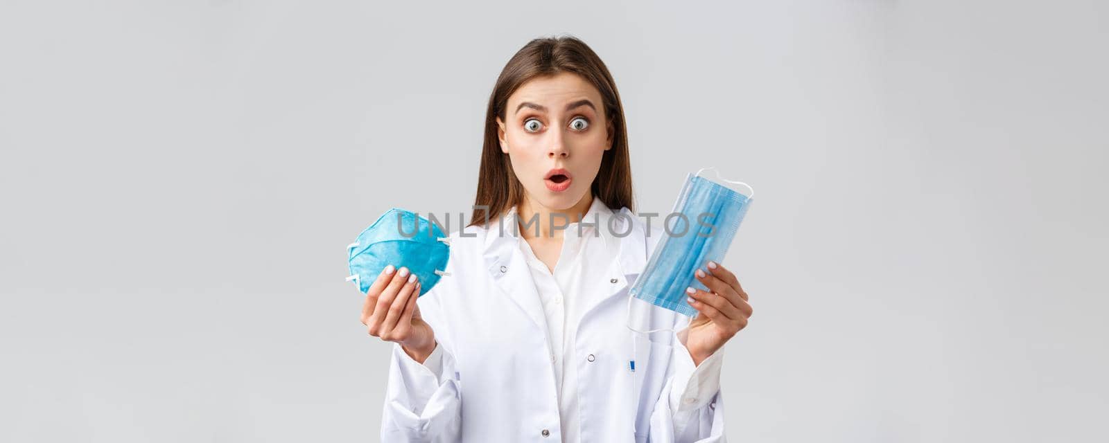 Covid-19, preventing virus, healthcare workers and quarantine concept. Surprised and shocked doctor in white scrubs, gasping and stare astonished, showing medical mask and respirator.