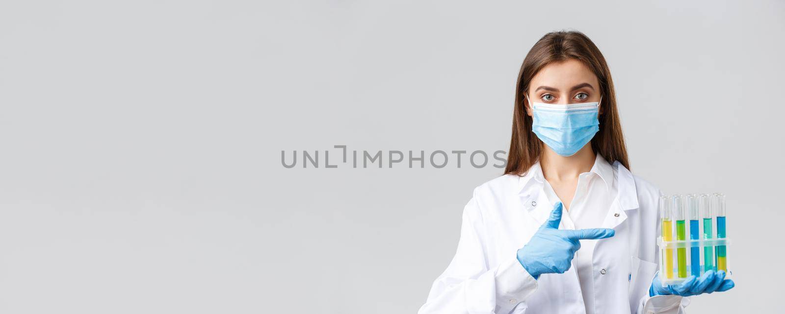 Covid-19, preventing virus, healthcare workers concept. Professional doctor in personal protective equipment, medical mask, pointing at test-tube with coronavirus vaccine, patient samples.