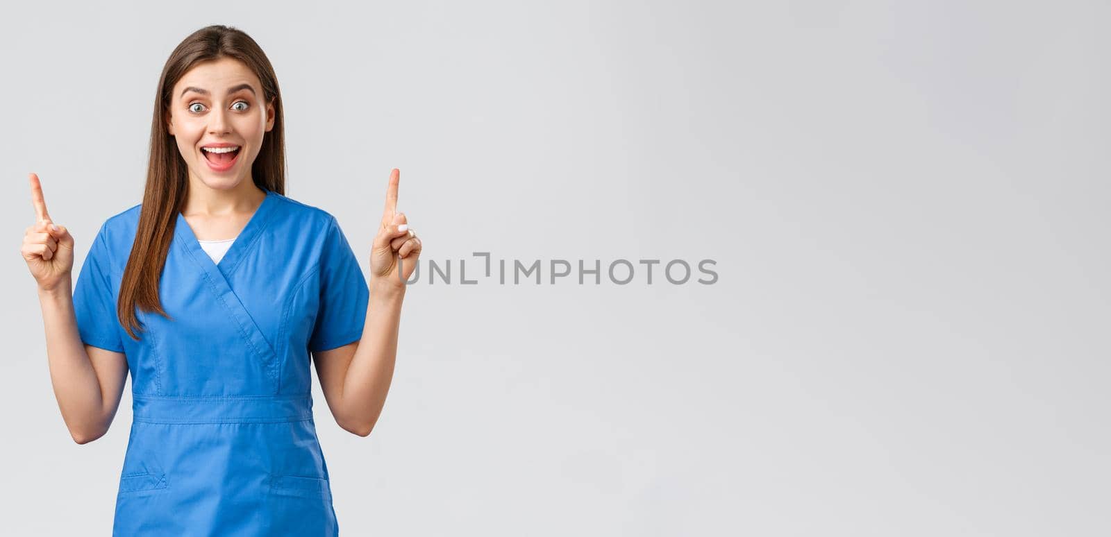 Healthcare workers, prevent virus, insurance and medicine concept. Excited, happy nurse or doctor in blue scrubs smiling from good news, pointing fingers up, show patients great news by Benzoix