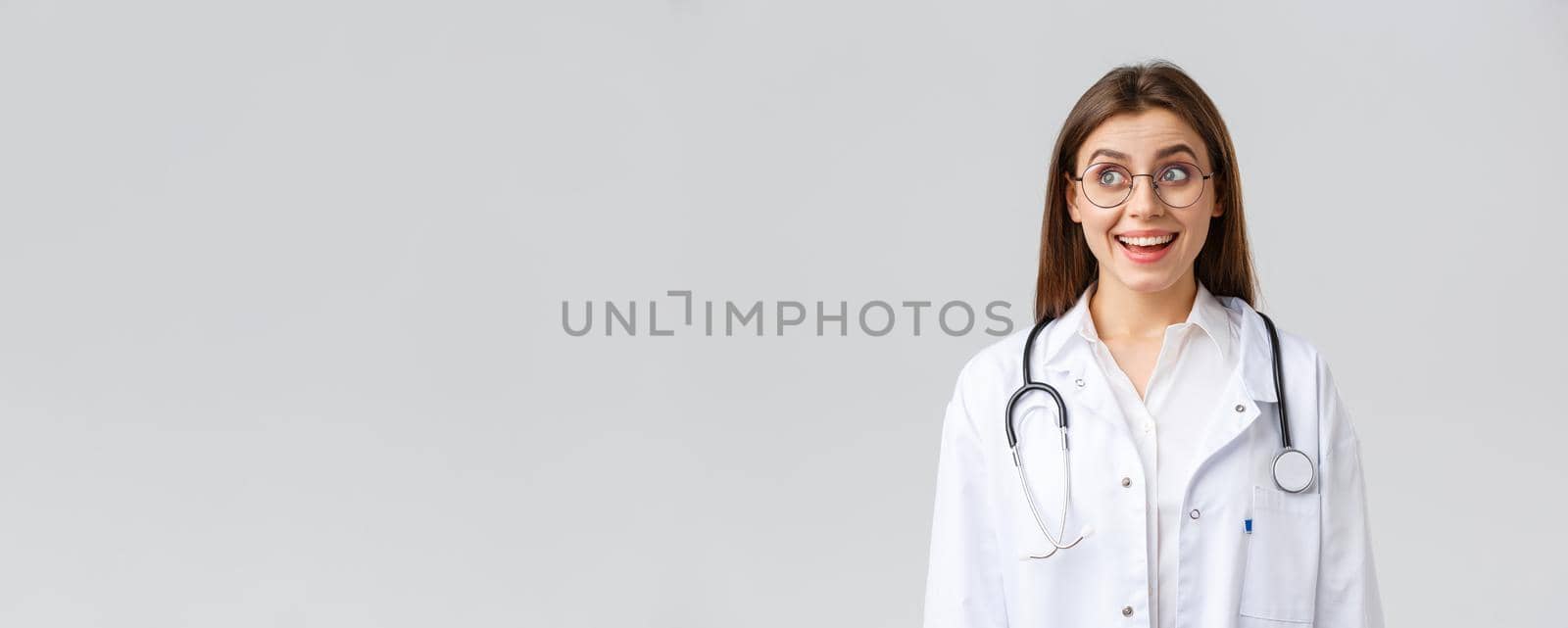 Healthcare workers, medicine, insurance and covid-19 pandemic concept. Happy optimistic female doctor, physician with stethoscope in white scrubs and glasses, look upper left corner with upbeat smile by Benzoix