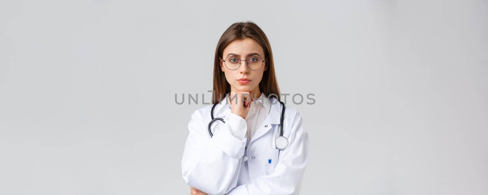 Healthcare workers, medicine, insurance and covid-19 pandemic concept. Serious smart, professional female doctor in glasses and white scrubs, thinking, taking decision or choice, look camera.