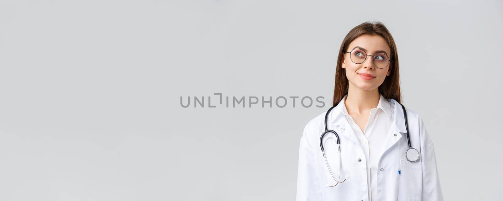 Healthcare workers, medicine, insurance and covid-19 pandemic concept. Dreamy young talented doctor in white scrubs and glasses, looking upper left corner thoughtful and smiling, imaging something by Benzoix