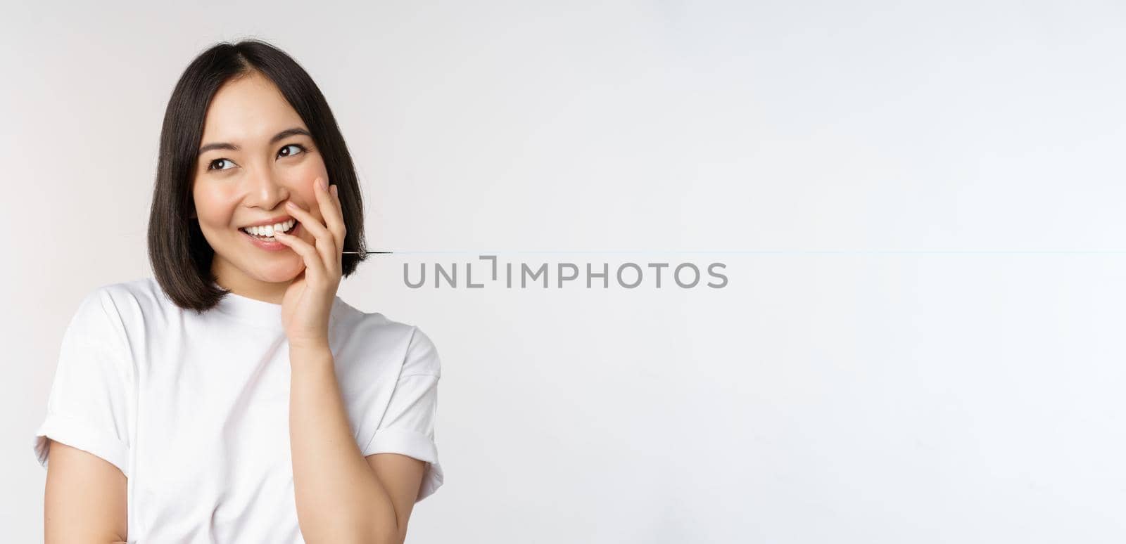 Portrait of young beautiful woman, korean girl laughing and smiling, looking coquettish, standing against white background.