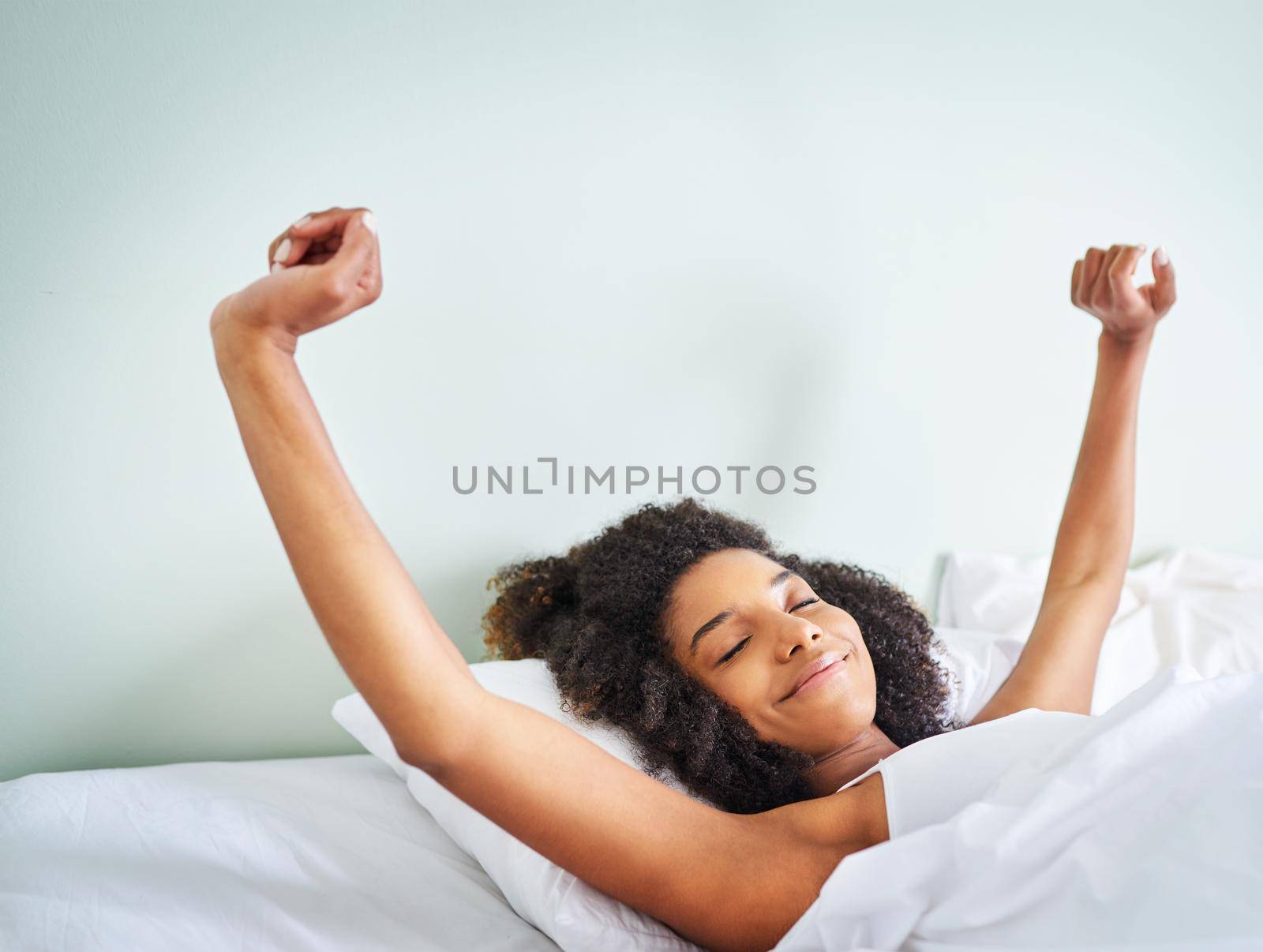 What a good night of rest. Shot of a cheerful young woman waking up after a good nights sleep in her bed at home during the day. by YuriArcurs