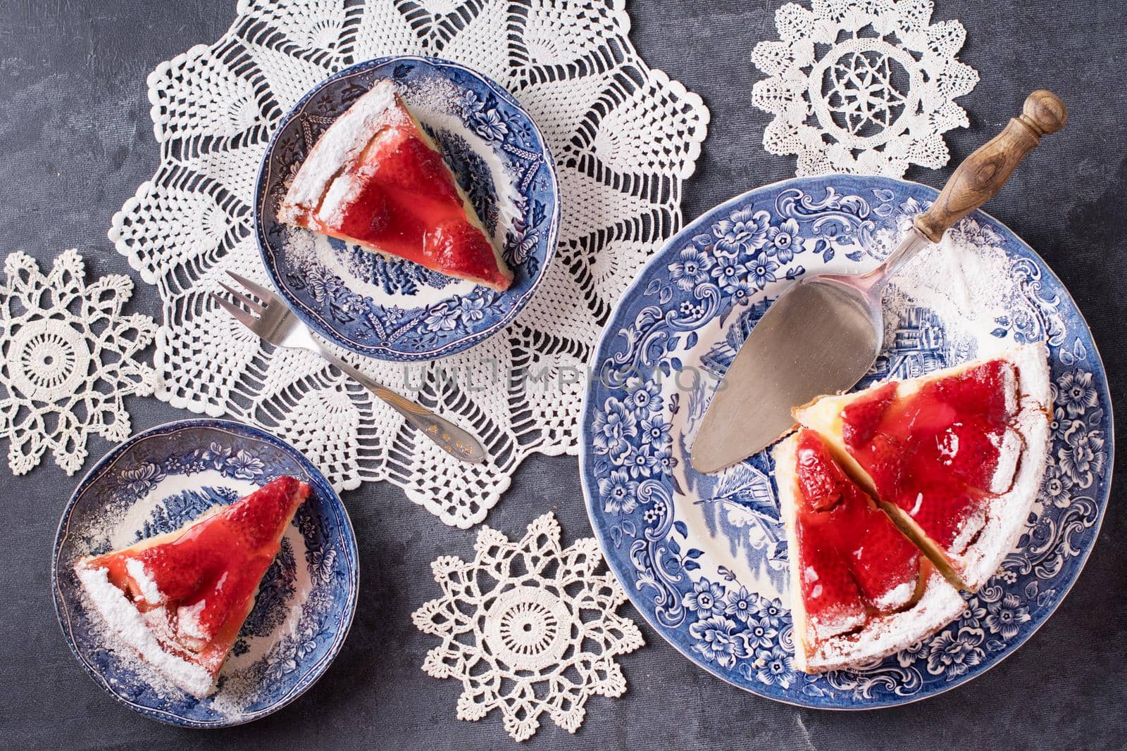 Christmas red strawberry pie on blue plates and a gift in a red box on the table, flat lay colorful food on white knitted napkins in the form of snowflakes, winter mood. High quality photo