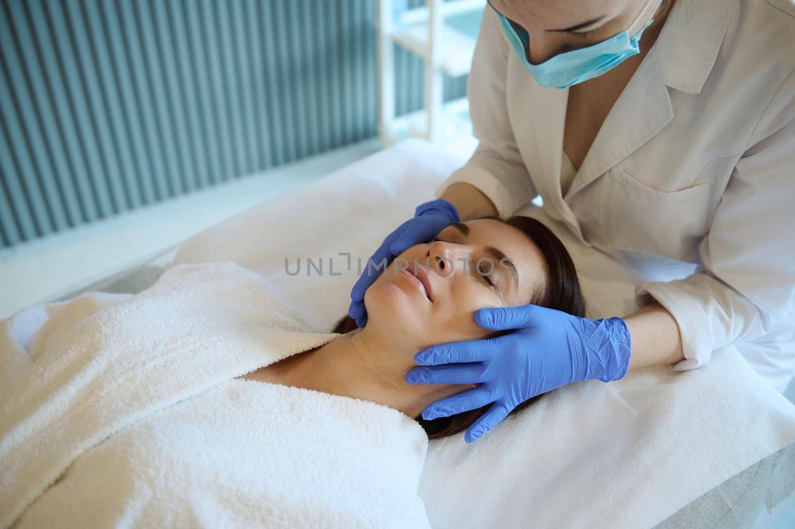 Beautiful middle-aged woman enjoying a professional smoothing rejuvenating facial massage while lying with her eyes closed on the couch. Enjoy wellness treatments at the spa and wellness center.