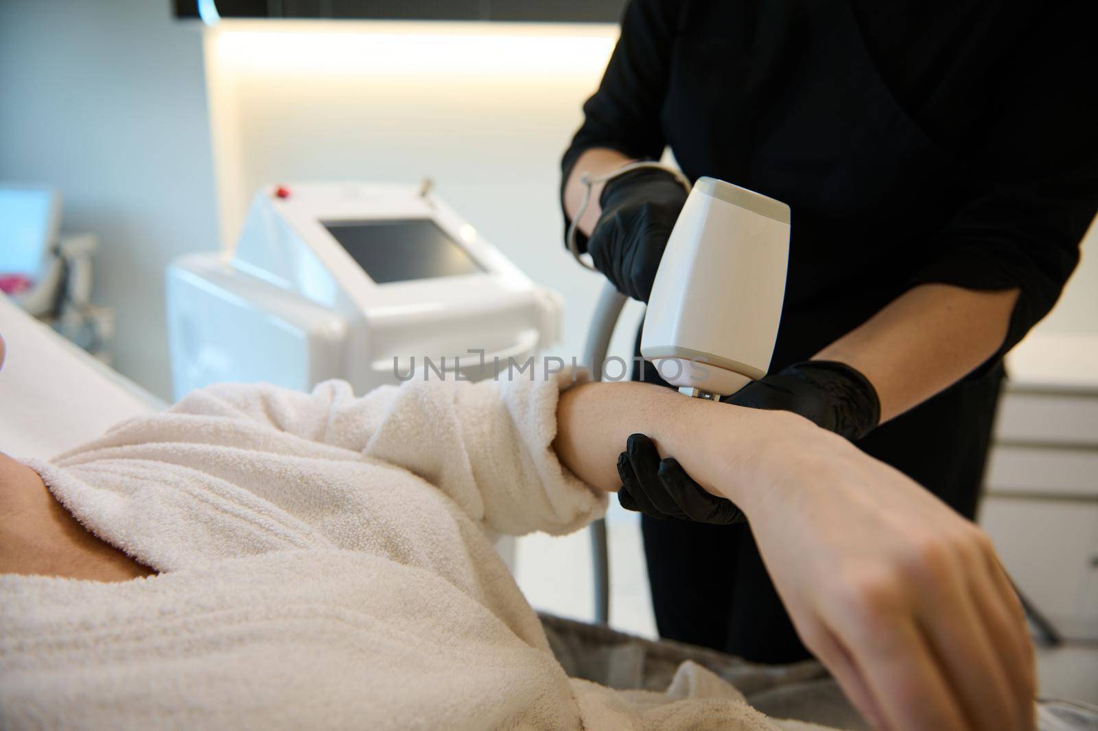 Close-up of an unrecognizable cosmetologist aesthetician performing a hair removal procedure on the hand of a woman with modern laser equipment in wellness spa clinic