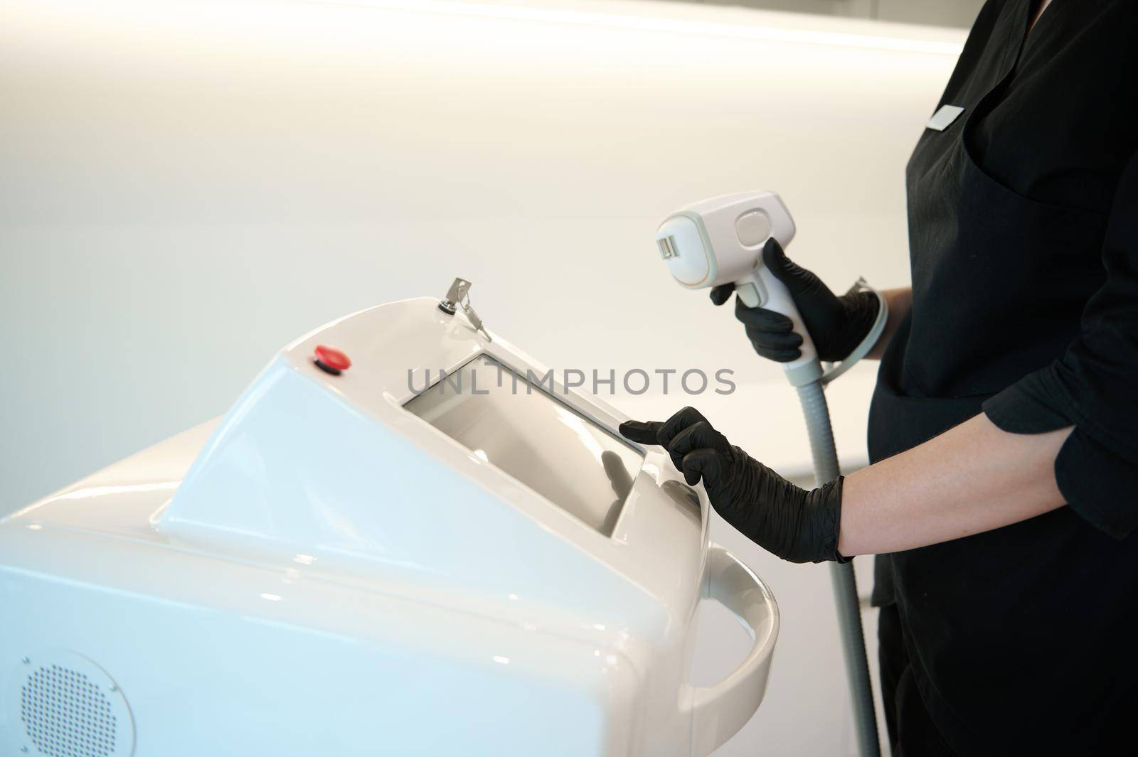 Apparatus for laser hair removal and the hands of a doctor-cosmetologist in medical black gloves, adjusting the settings on the monitor screen of a modern laser device. Epilation and spa concept by artgf