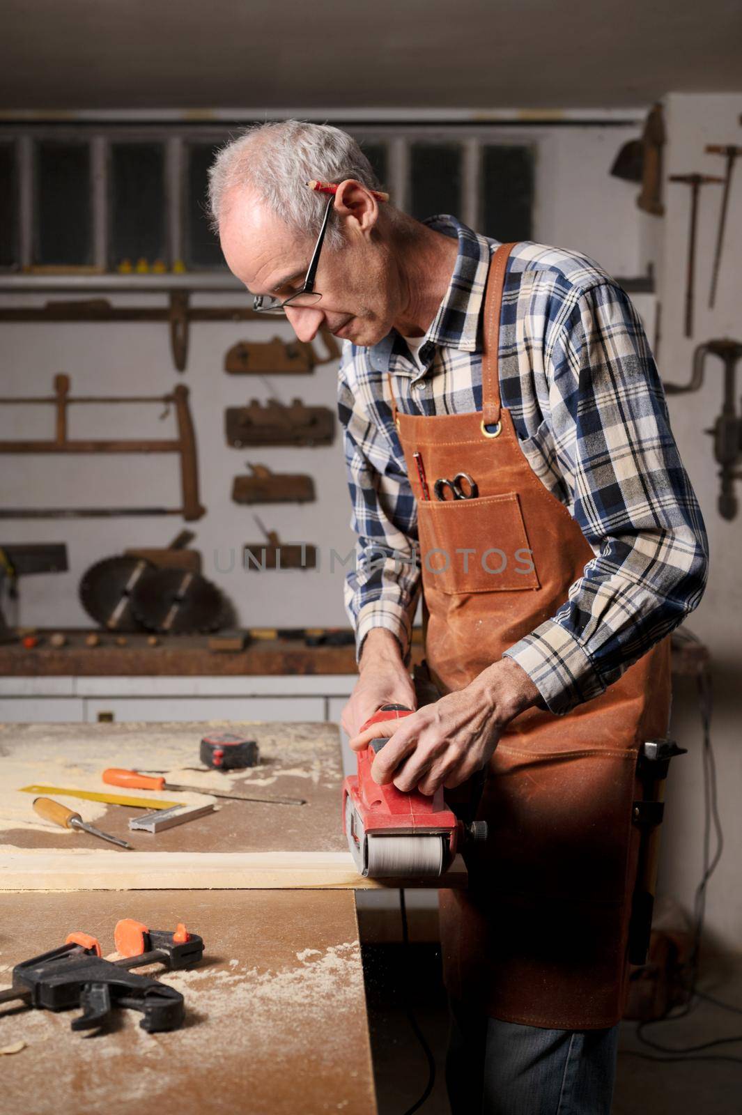 Carpenter sanding wood with belt sander at workshop in wooden board project or woodworking carpentry by HERRAEZ