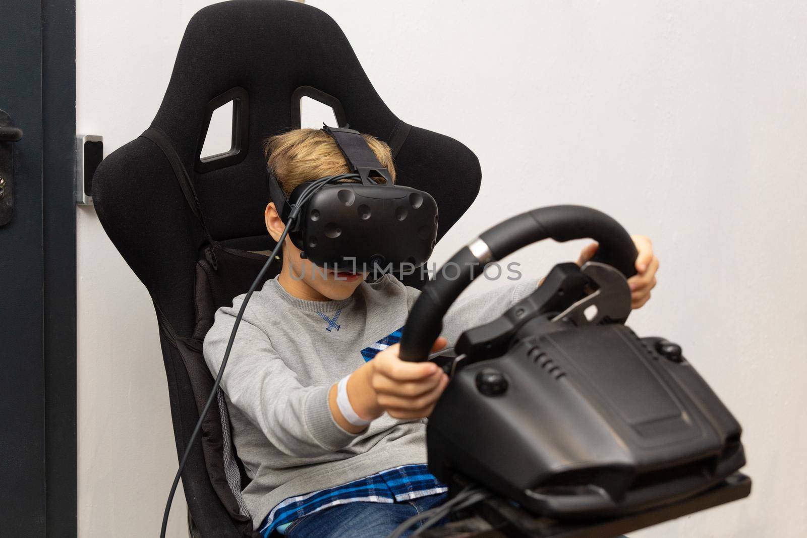 The boy plays on the racing simulator in glasses of a virtual reality on white background. Virtual reality on car simulator