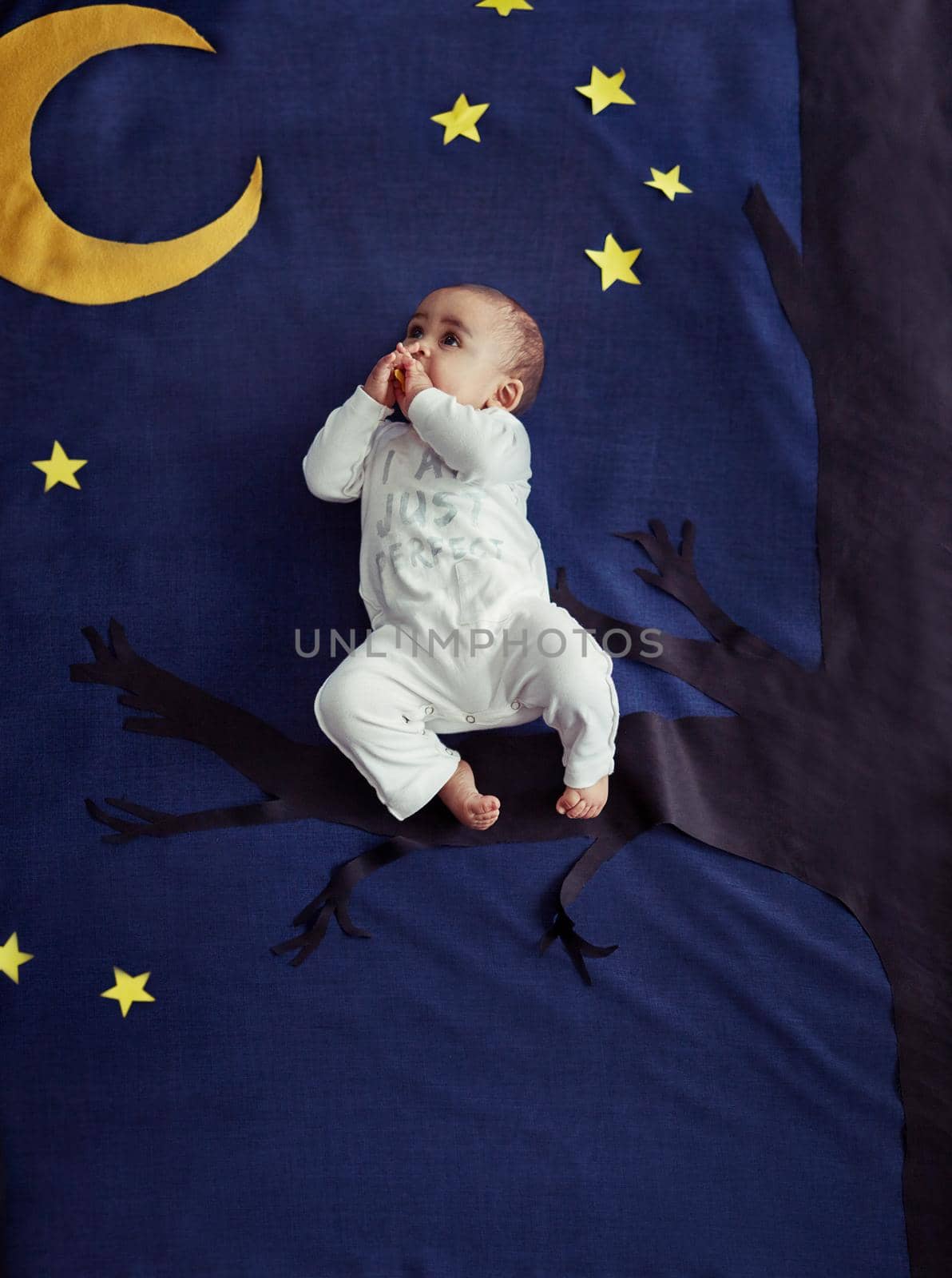 Concept shot of an adorable baby boy sitting on a tree against an imaginary night time background.