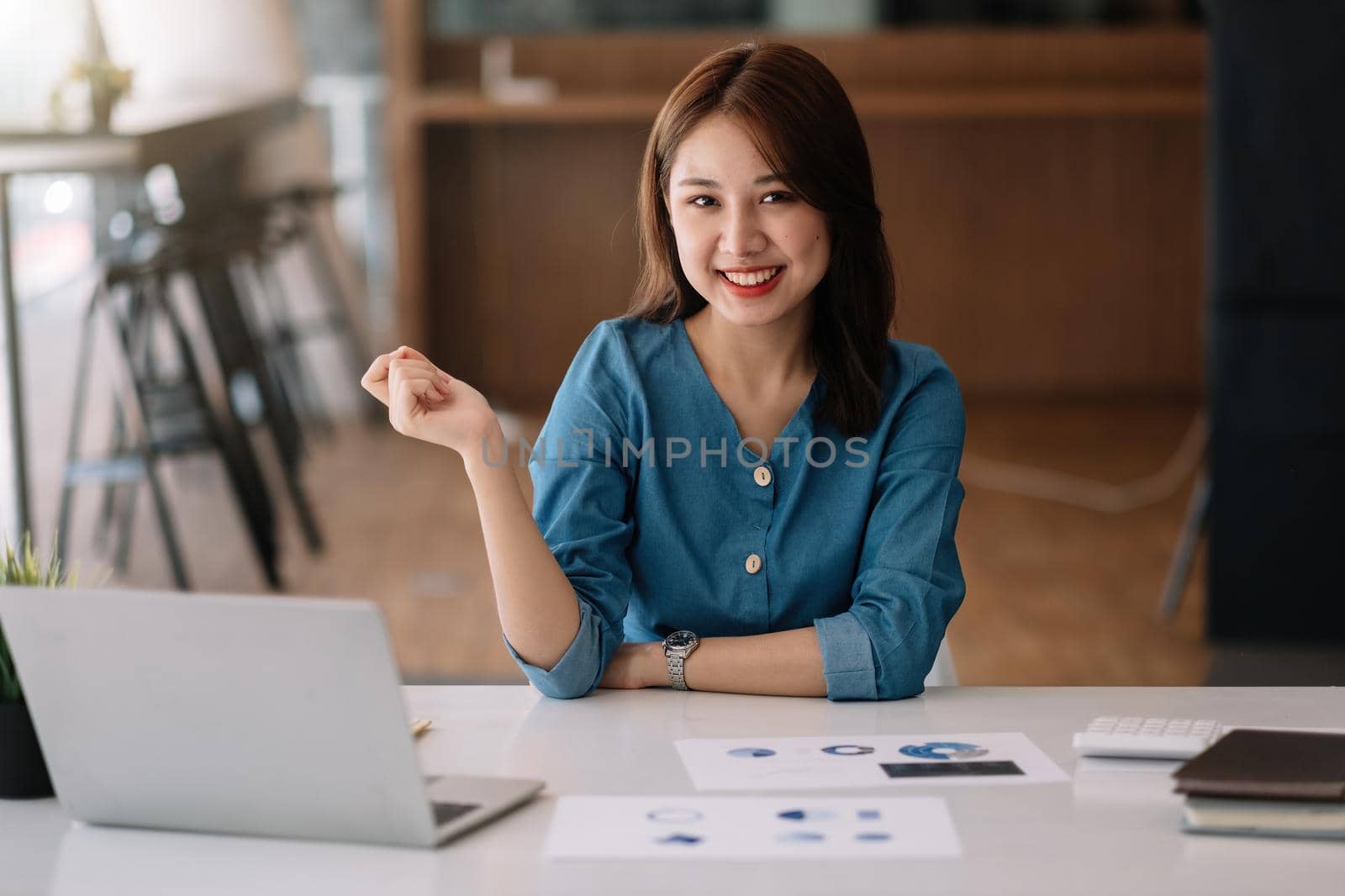 Young chariming asian woman using her laptop while sitting in a chair at her working place. she looking at camera