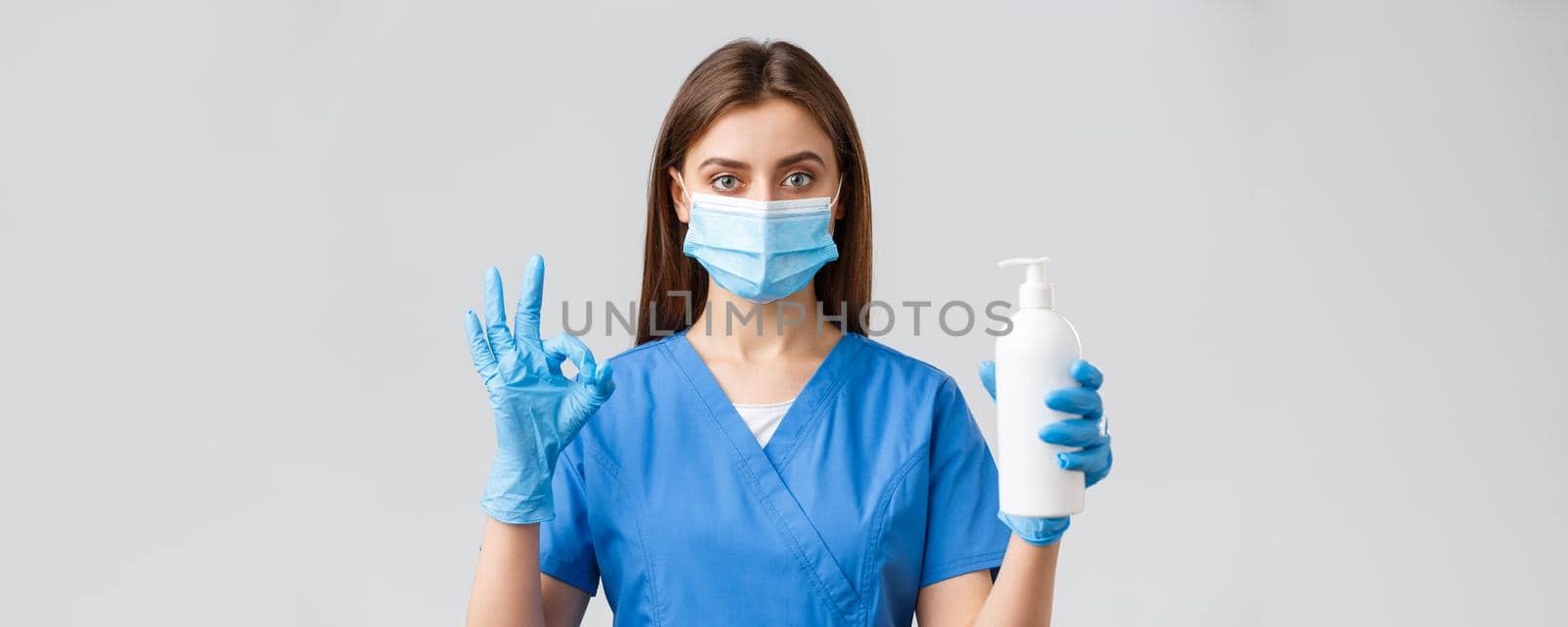 Covid-19, preventing virus, health, healthcare workers and quarantine concept. Confident serious female nurse, pretty doctor in scrubs and medical mask, show hand sanitizer, soap and okay sign.