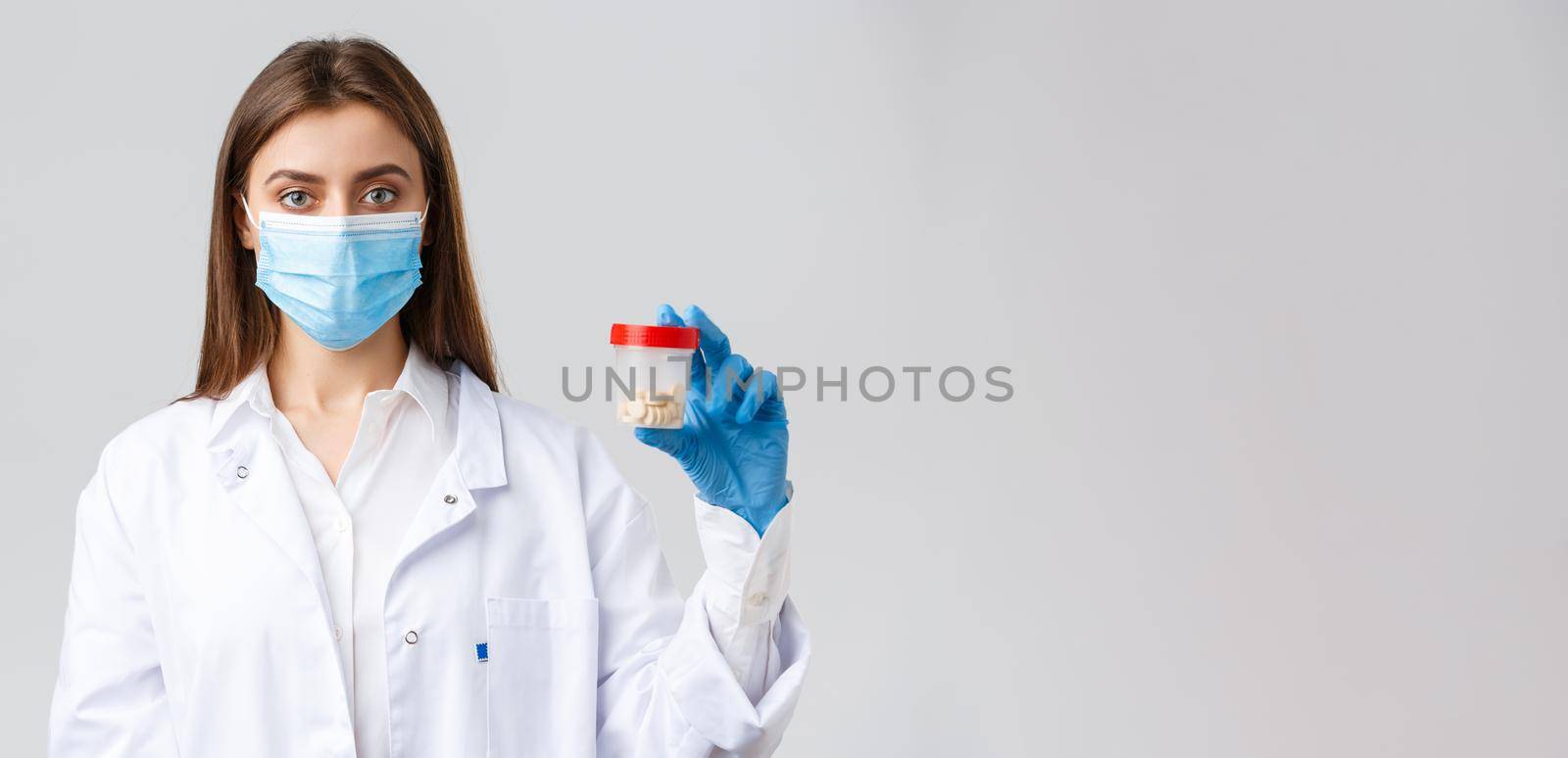 Covid-19, preventing virus, healthcare workers and quarantine concept. Doctor in scrubs and medical mask, showing container with pills, recommend vitamins or antibiotics.