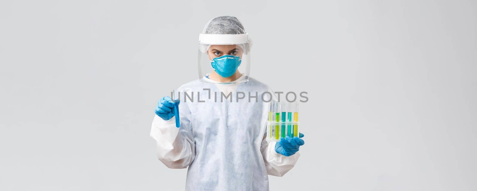 Covid-19, medical research, diagnosis, healthcare workers and quarantine concept. Doctor in personal protective equipment hold test-tubes with coronavirus vaccines, working in clinic laboratory by Benzoix