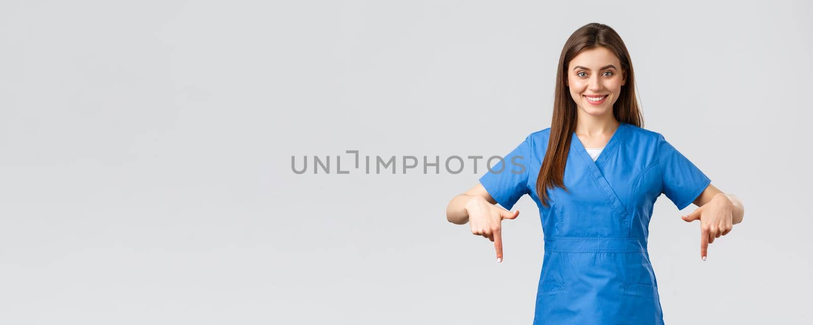 Healthcare workers, prevent virus, covid-19 test screening, medicine concept. Smiling confident nurse, doctor or intern in blue scrubs, pointing fingers down as give patients information by Benzoix