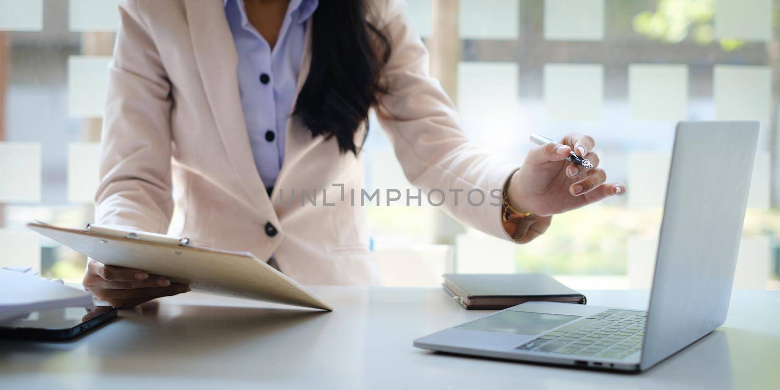 Business woman hand holding pencil and financial paperwork looking at bank savings account application on laptop computer. account or saving money or insurance concept