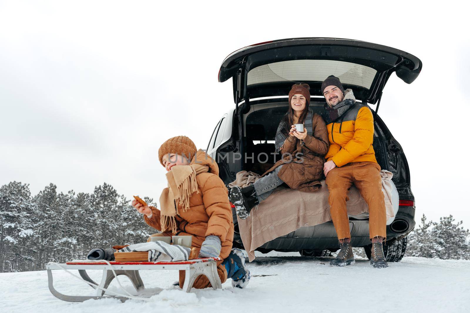 Winter portrait of a family sit on car trunk enjoy their vacation in snowy forest