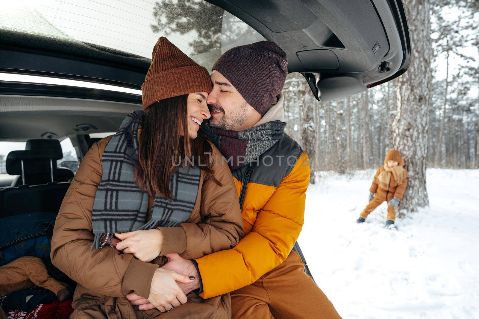 Lovely smiling couple sitting in car trunk in winter forest, close up