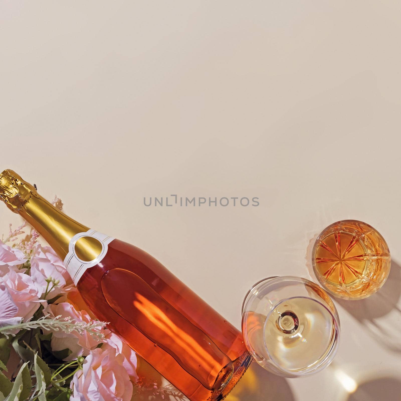 Festive arrangement with flowers and a bottle of champagne next to full two glasses filled with alcoholic drink as birthday or anniversary card with copy space