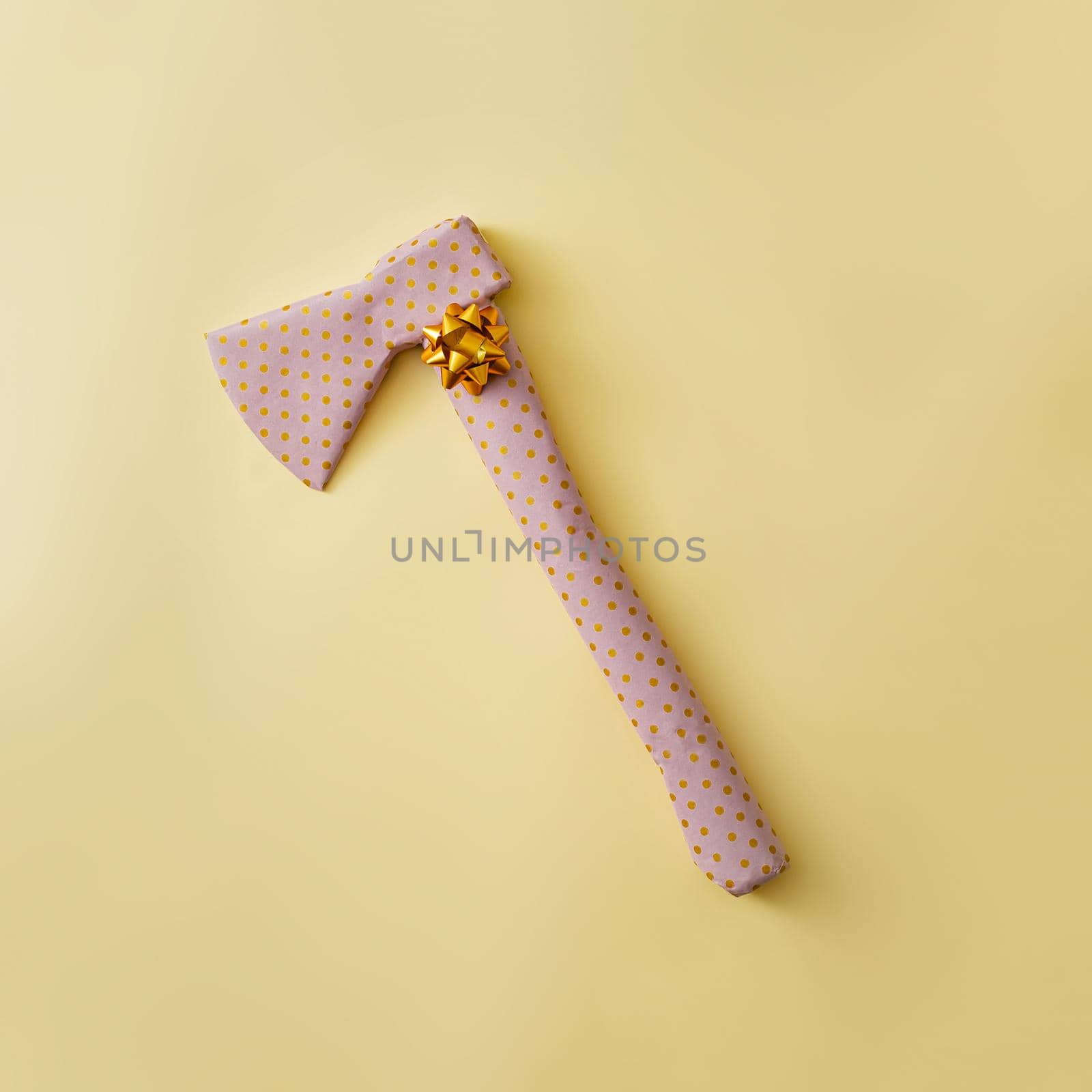 An ax wrapped as a gift with a golden bow. Joke concept and pastel color.
