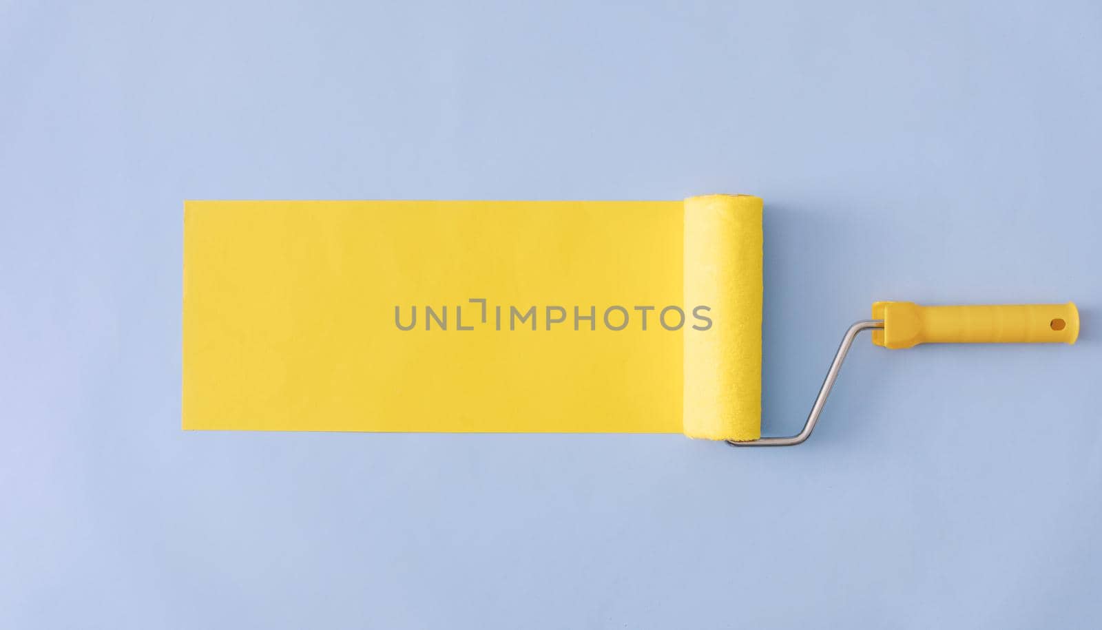Yellow painted banner with paint roller and copy space over a blue background in a wide angle panorama