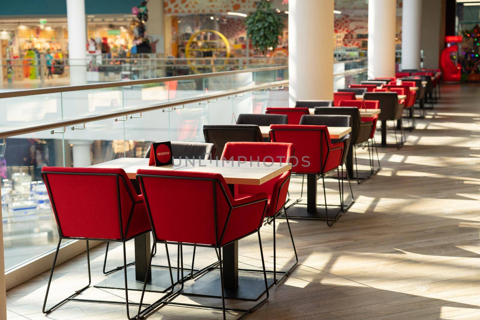 A row of tables with soft chairs for visitors to the food court of a modern shopping center. People admire the beautiful view during the meal.