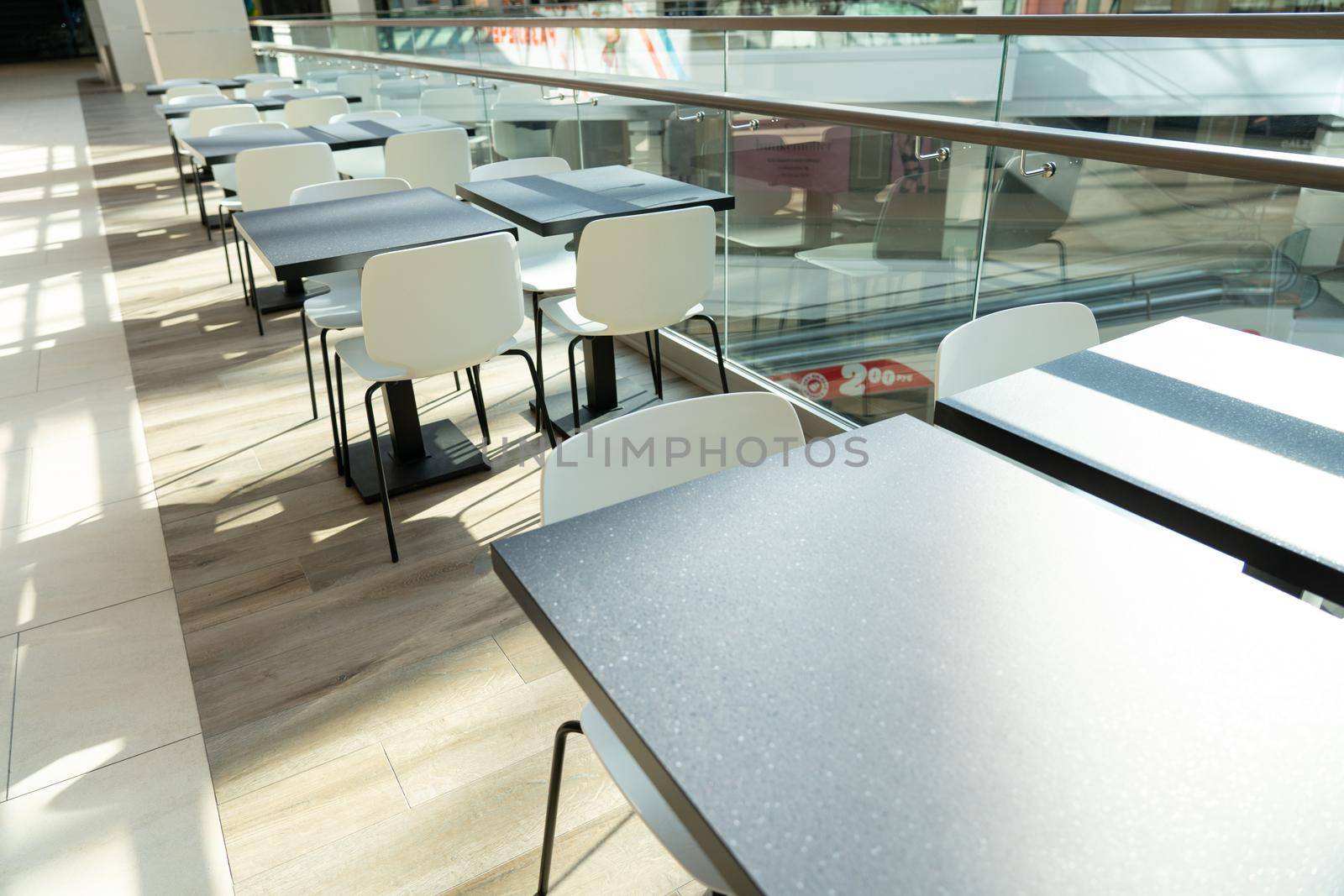 A row of tables with white chairs for visitors to the food court of a modern shopping center. People admire the beautiful view during the meal.