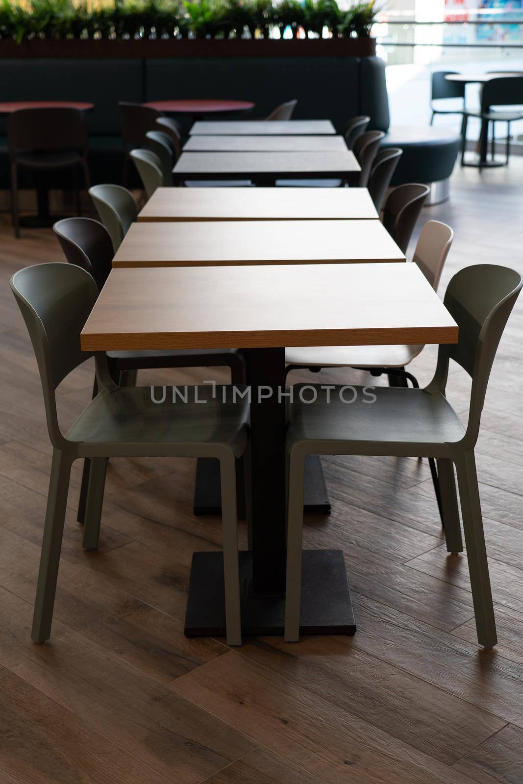 A row of tables with white chairs for visitors to the food court of a modern shopping center. People admire the beautiful view during the meal.