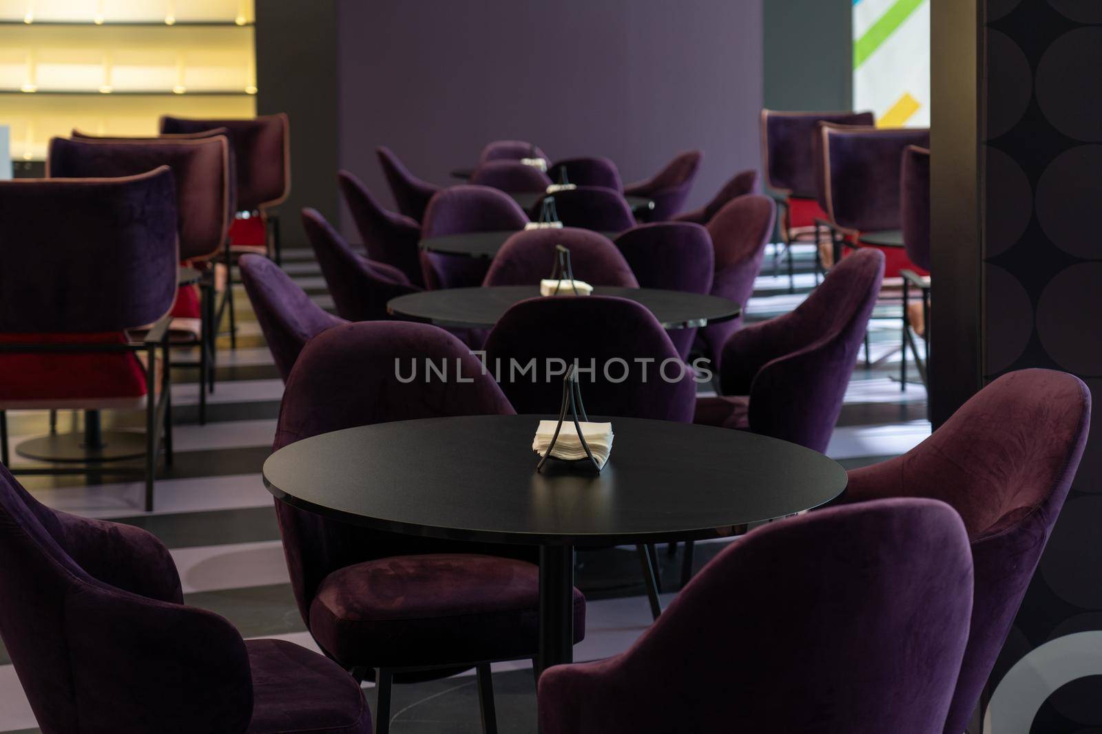 A row of tables with soft comfortable violet chairs for visitors to the food court of a modern shopping center. People admire the beautiful view during the meal.