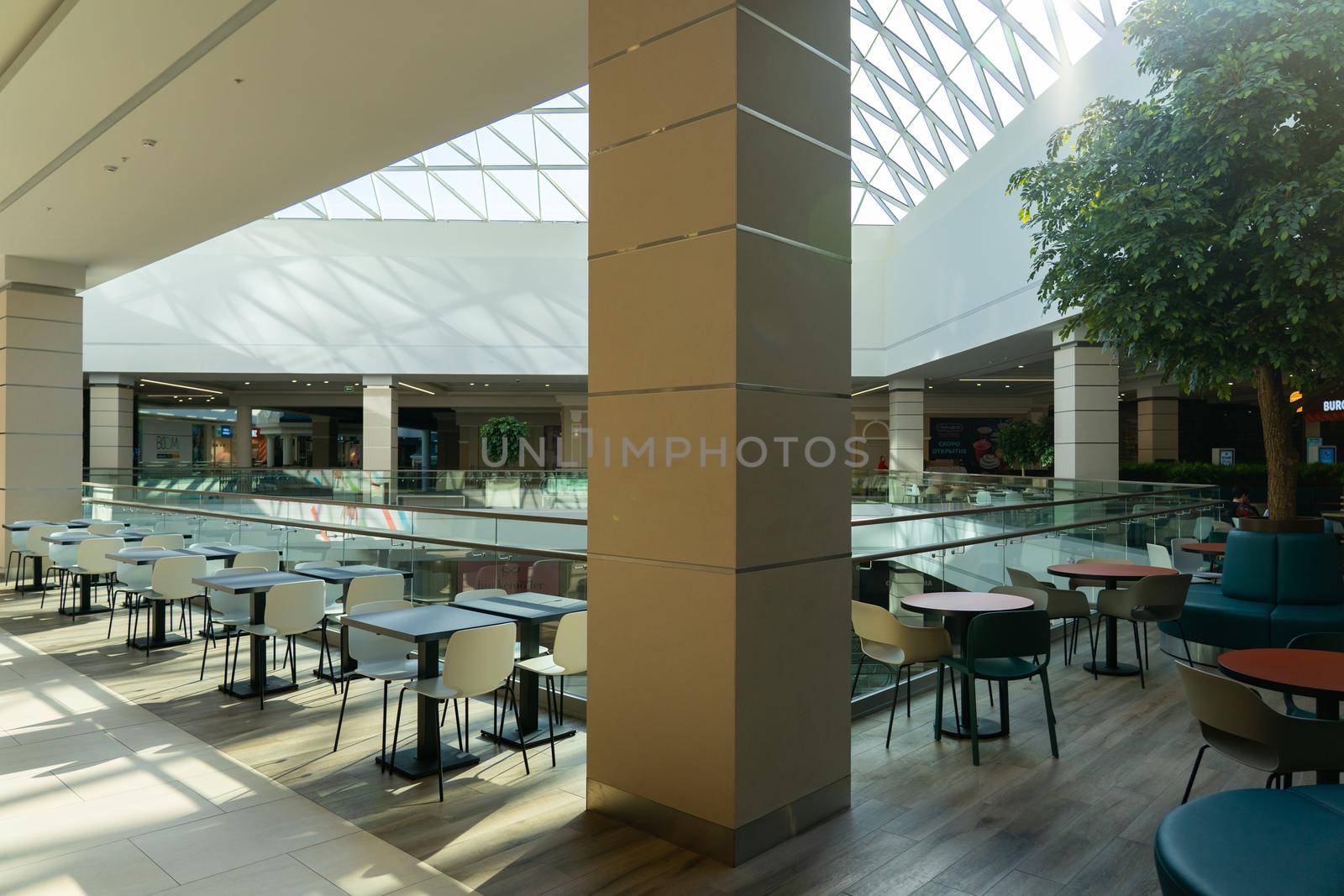 Grodno, Belarus - April 07, 2021: A row of tables with white chairs for visitors to the food court of a modern shopping center Triniti. People admire the beautiful view during the meal.