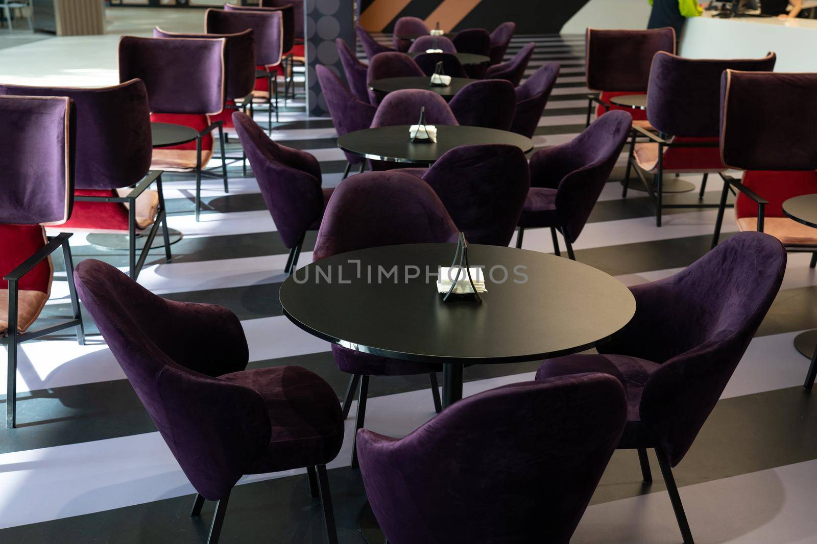 A row of tables with soft comfortable violet chairs for visitors to the food court of a modern shopping center. People admire the beautiful view during the meal.