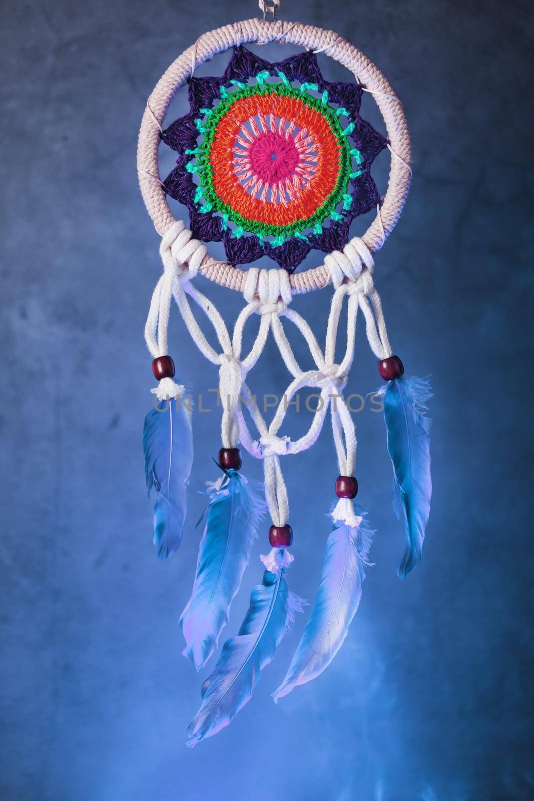 Dreamcatcher with multicolored weaving in blue smoke isolated on black by AlexGrec