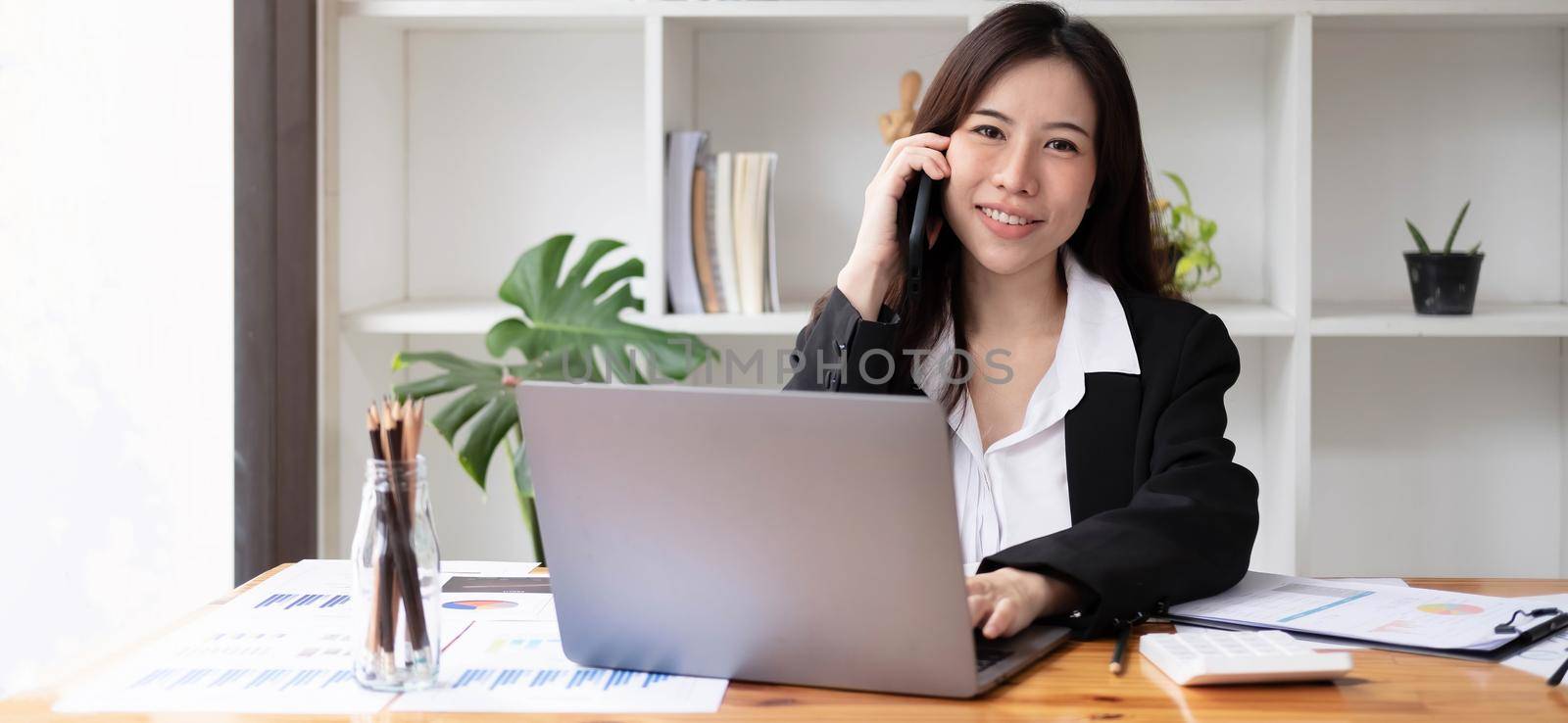 Business asian woman using smartphone for do math finance on wooden desk in office, tax, accounting, financial concept.