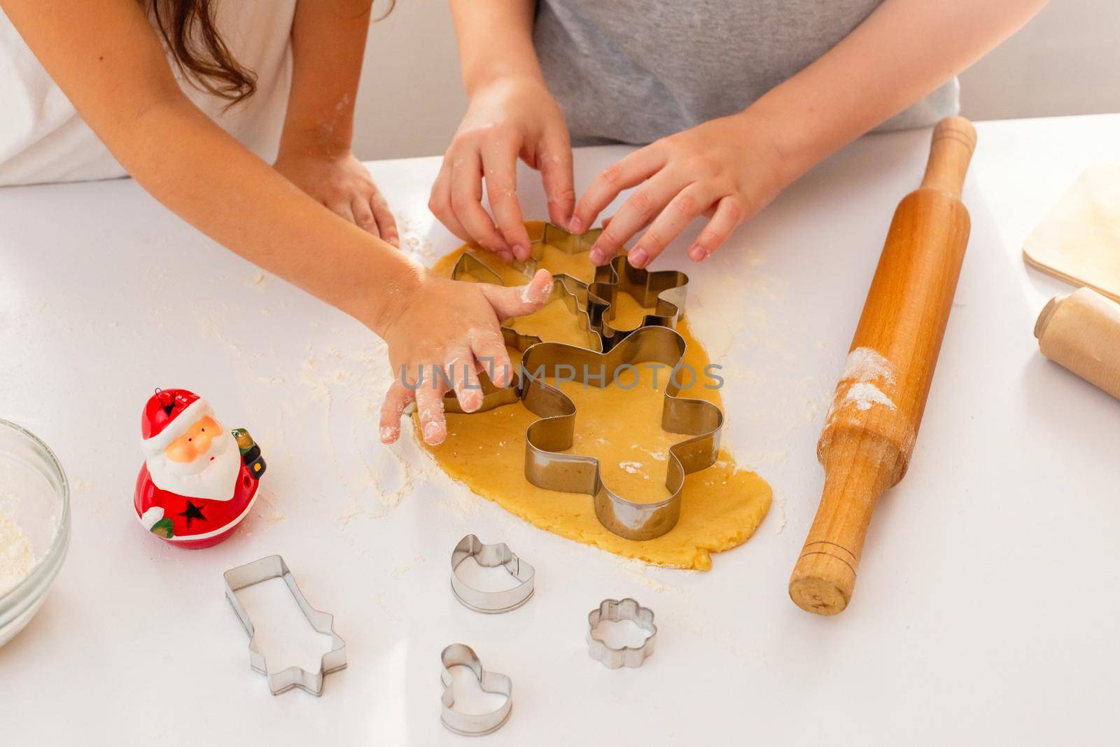 Children's hands, close-up, on a white table, cut out from the dough Christmas figured cookies in the form of a man, a Christmas tree and other figures. Top view