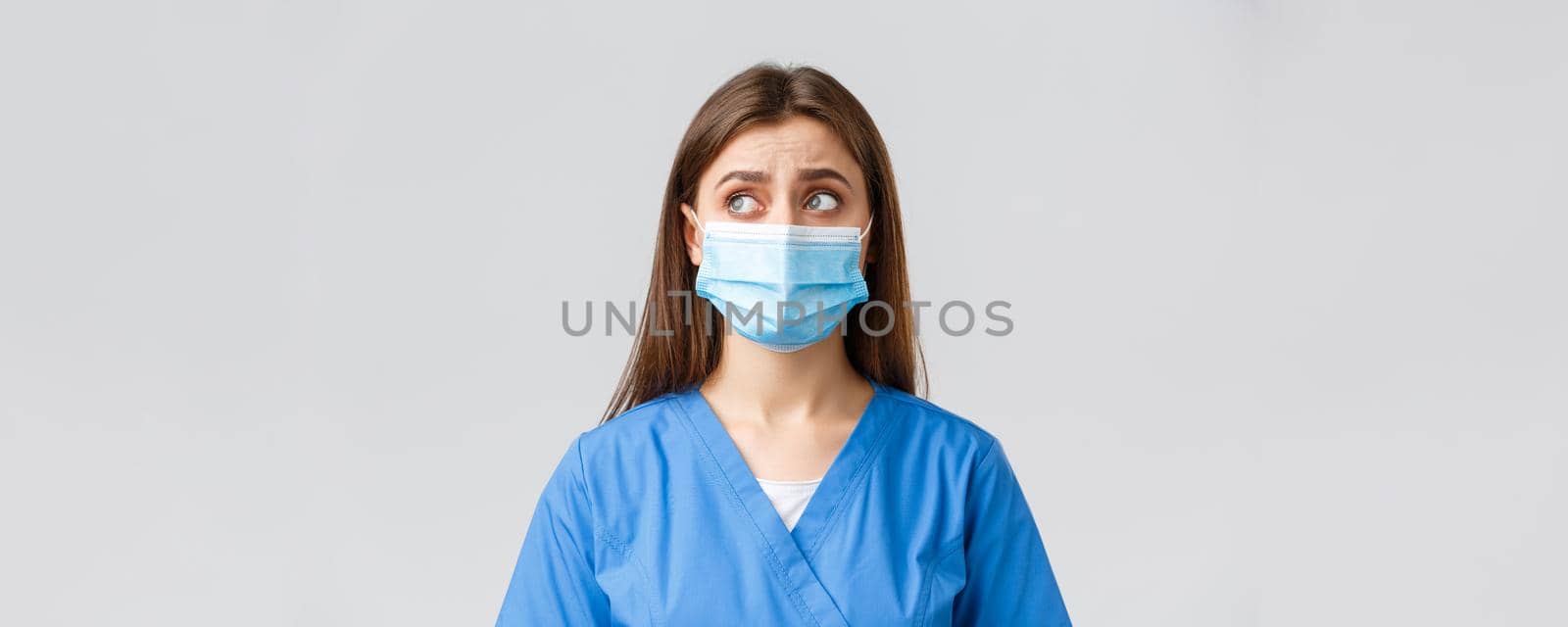 Covid-19, preventing virus, health, healthcare workers and quarantine concept. Skeptical distressed female nurse or doctor in blue scrubs, medical mask, look upper left corner uncertain or puzzled.